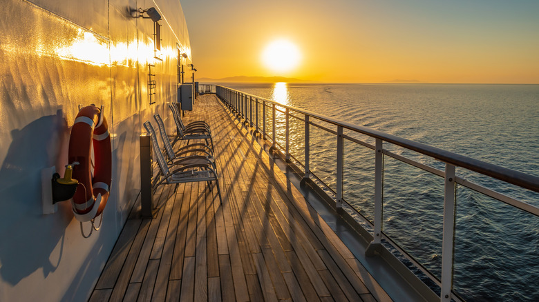 A side view of a cruise ship's deck while at sea featuring chairs and a life preserver on the side of the wall