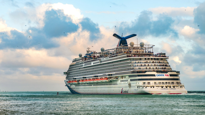 A Carnival Cruise ship sails on the water with clouds and a blue sky behind it.