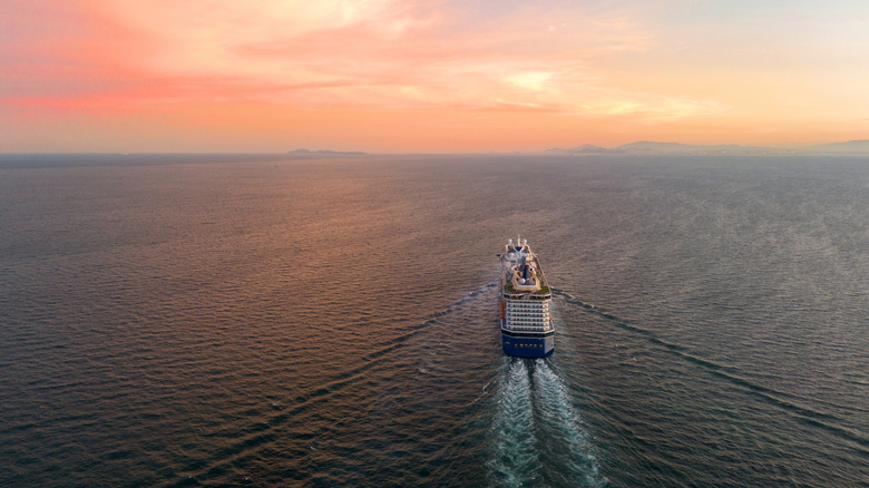 A cruise ship sails on the water heading towards an orange sky