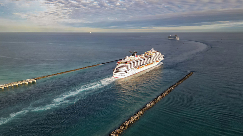A white cruise ships sails in the ocean with another ship behind it