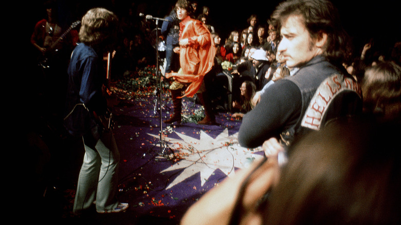 A man in a Hells Angels jacket guards the stage while the Rolling Stone perform at Altamont