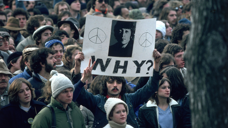 A crowd of mourners for John Lennon with one holding up a sign asking "why?"