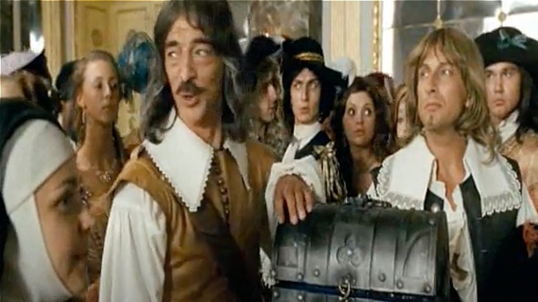 extras making faces behind musketeers with treasure chest