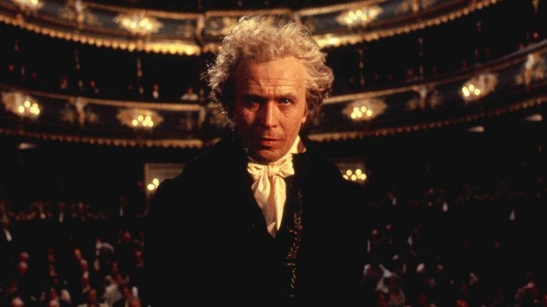 Gary Oldman as Beethoven in dark suit standing in concert hall in a still from Immortal Beloved