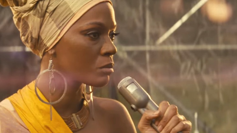 Zoe Saldaña as Nina Simone in yellow headdress holding mic in a still from Nina