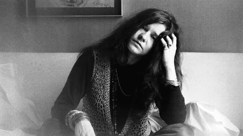 Janis Joplin sat on bed with hand raised to head