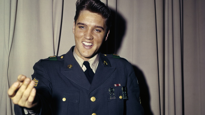 Elvis Presley smiling in front of a curtain in his army uniform