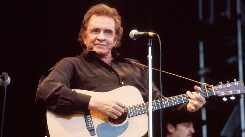 An elderly Johnny Cash strumming a guitar on stage