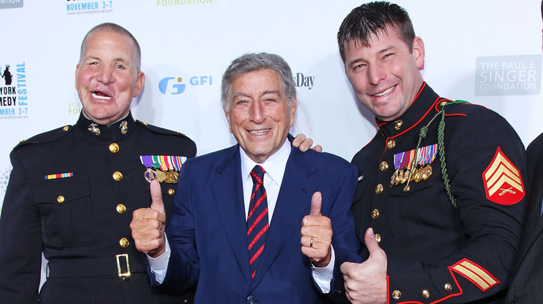 Tony Bennett giving a double thumbs up with two servicemen on the red carpet at a benefit