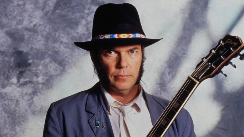 Neil Young posing while wearing black hat with guitar