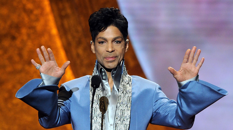 Prince on stage in blue suit holding hands up