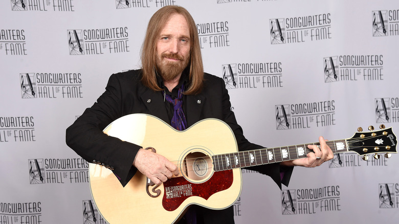 Tom Petty smiling in dark suit holding a guitar at an event