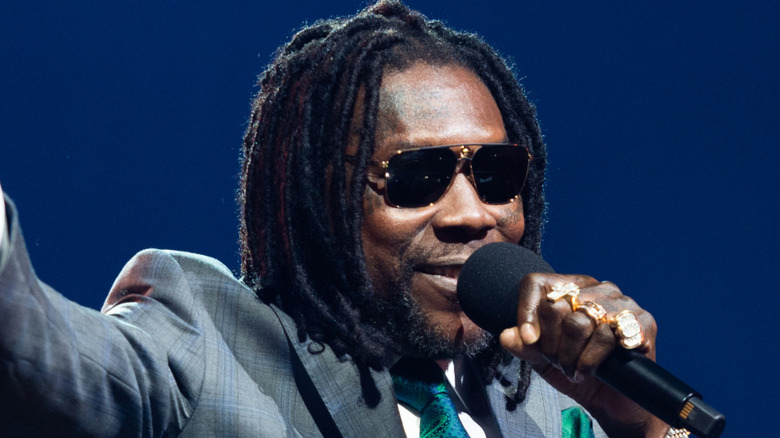 Vybz Kartel smiling in sunglasses while holding mic