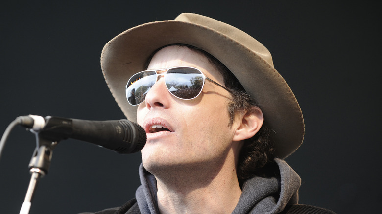 Jakob Dylan wearing sunglasses and a hat while singing into a microphone