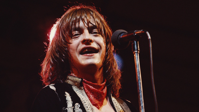 Rick Derringer smiling with a microphone on stage