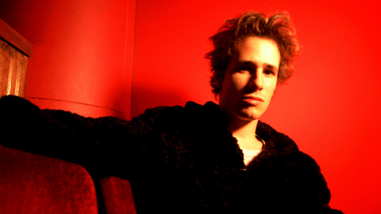 Singer Jeff Buckley posing in front of a red background
