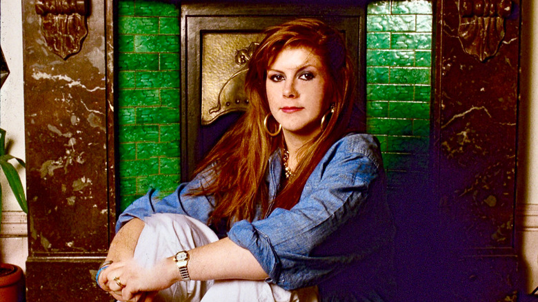 Singer Kirsty McColl posing in front of a fireplace
