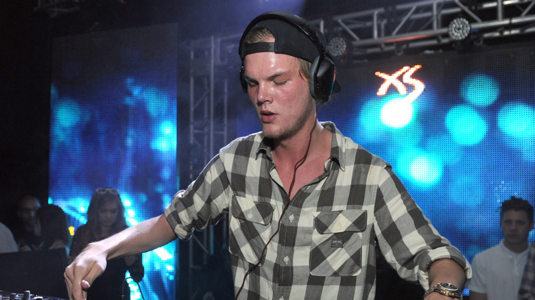 Avicii wearing headphones DJing in club