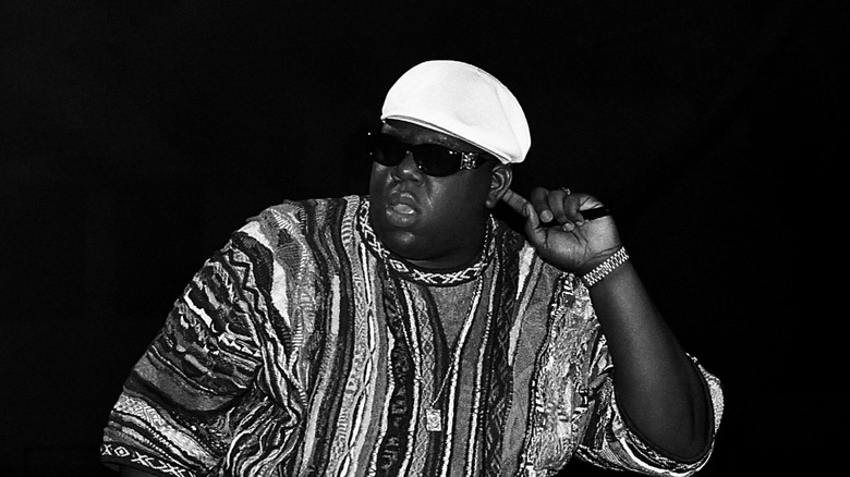 biggie smalls in white hat hand to ear with black background
