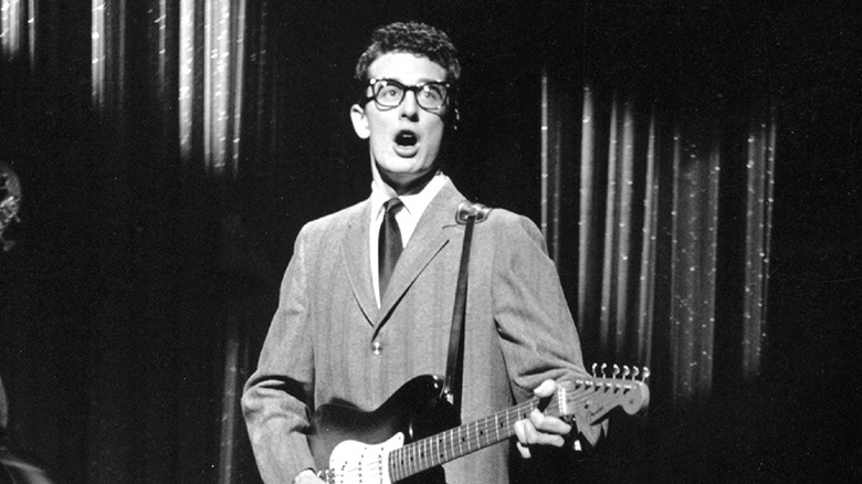 Buddy Olly in glasses and jacket playing guitar on stage