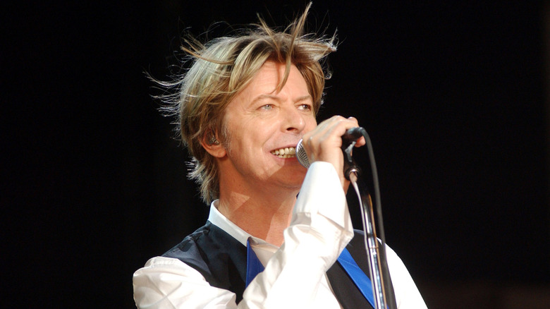 David Bowie on stage singing into a microphone with tussled hair.