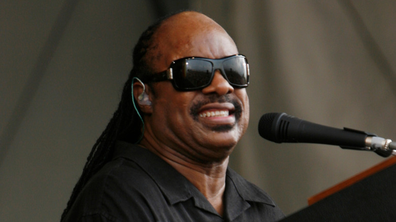 Stevie Wonder performing on stage, playing piano while grimacing into the microphone.