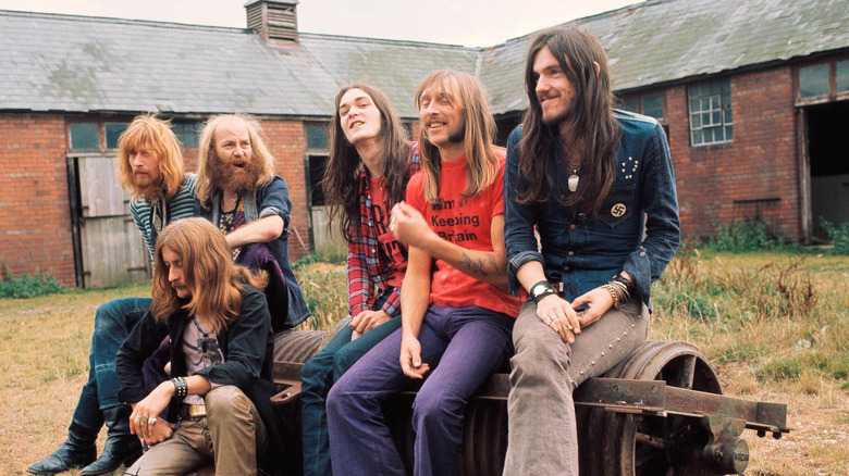 The members of the band Hawkwind seated on industrial equipment in front of a warehouse.