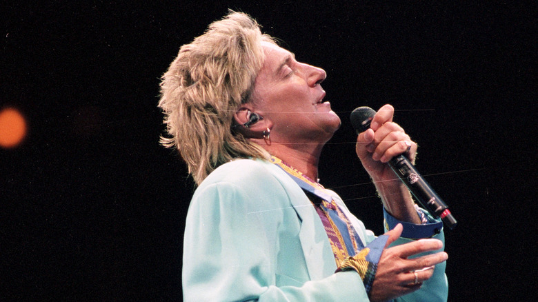 Rod Stewart in blue coat singing on stage in 1994