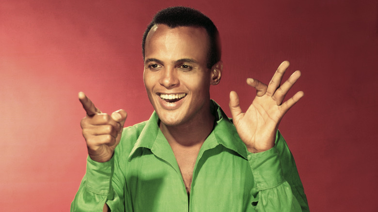 Harry Belafonte smiling and gesturing with both hands against red backgrounds