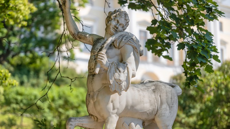 A statue of a centaur raising its arm in a sunny garden