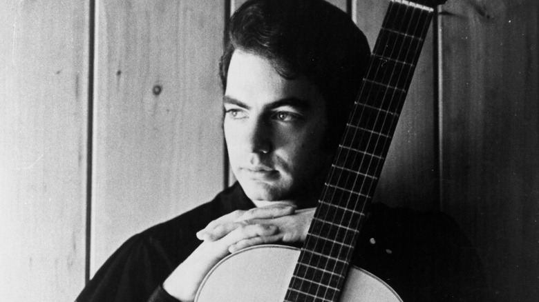 Neil Diamond in 1968 posing with hands folded on an acoustic guitar