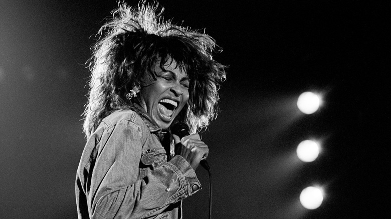 Tina Turner smiling and posing in front of a blue background
