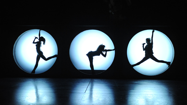 Female performers singing and striking poses in lit circles on stage