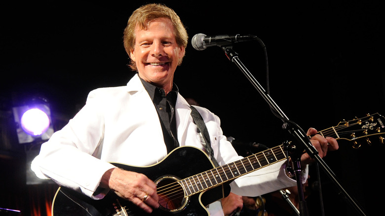 Ron Dante smiling in white suit playing guitar on stage