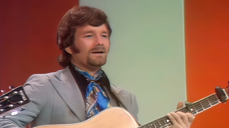 Rick Evans in grey suit playing guitar and singing on stage