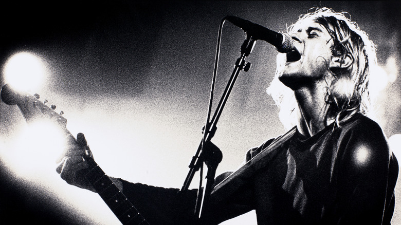 Kurt Cobain playing guitar and singing into microphone