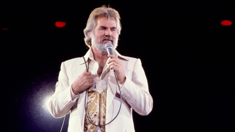 Kenny Rogers singing into microphone in white suit jacket