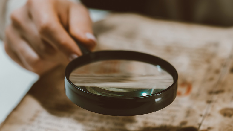 Hand holding magnifying glass over old paper