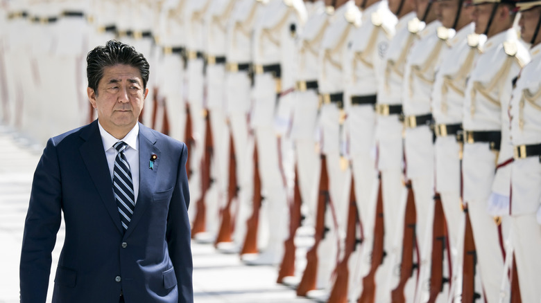 Shinzo Abe in suit walking in front of Japanese troops