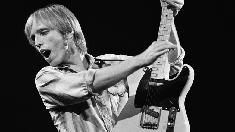 Tom Petty singing and holding up guitar on stage