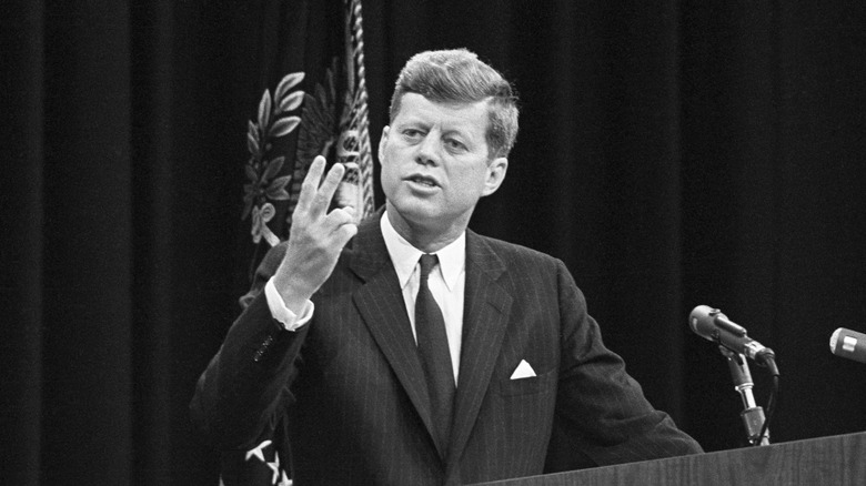 President John F. Kennedy speaking at press conference holding up fingers