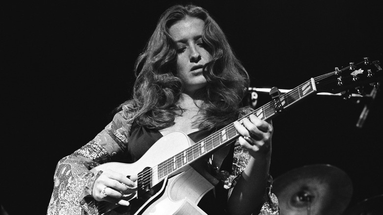 Black and white photo of Bonnie Raitt playing the guitar in a paisley printed top during a concert in San Francisco in the late '70s