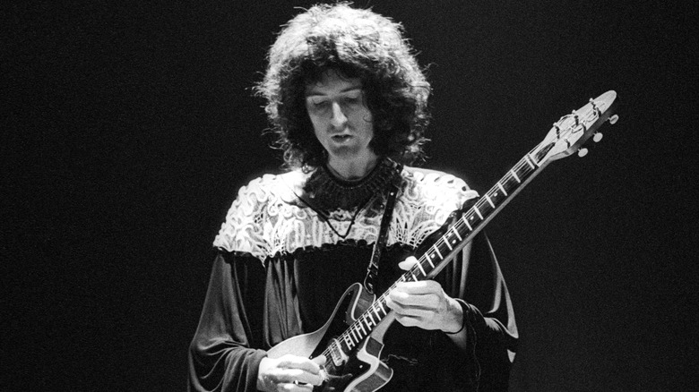 Brian May playing electric guitar in a black gown