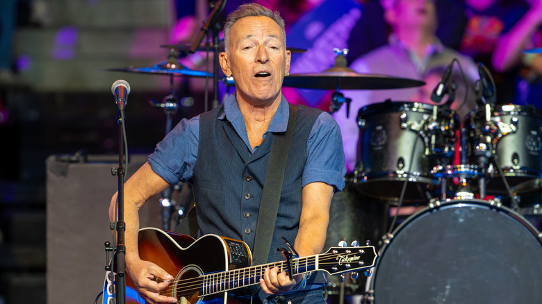 Bruce Springsteen playing an acoustic guitar on stage with a band