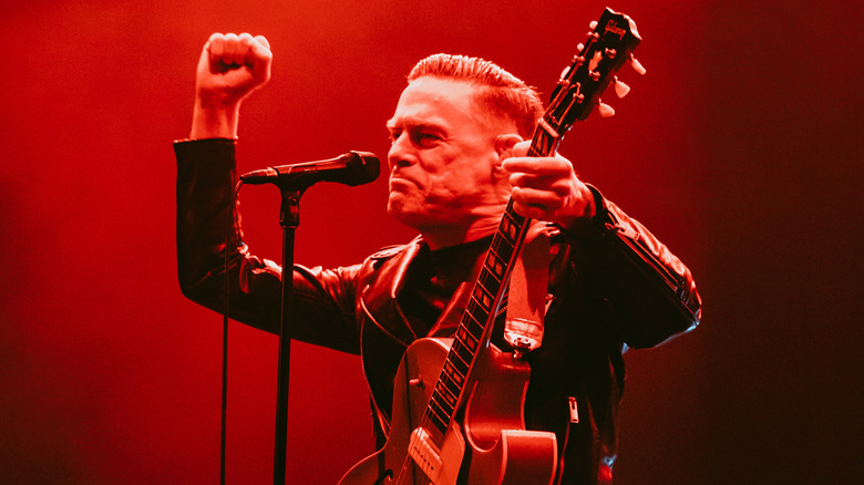 Bryan Adams smiling pumping fist with guitar on stage