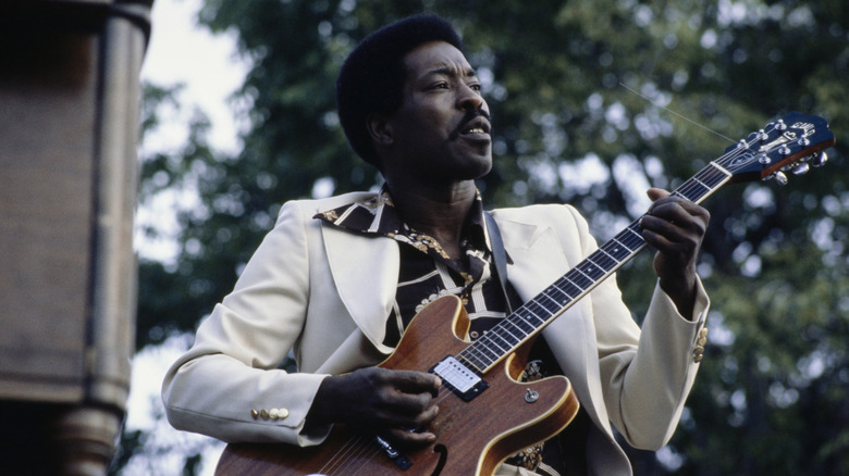 Buddy Guy in white suit jacket playing guitar outdoors