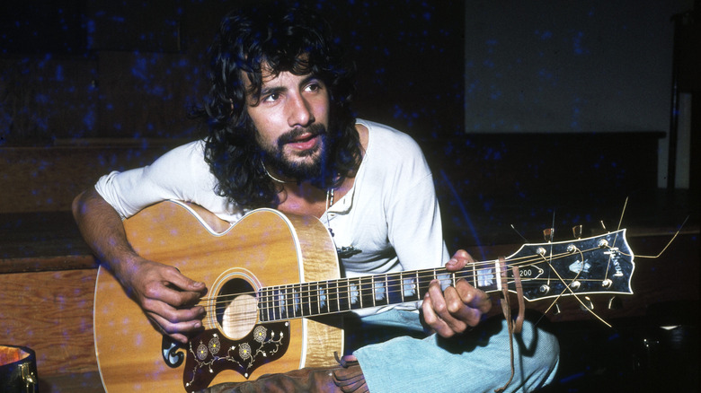 Cat Stevens/Yusuf Islam seated, playing a guitar.