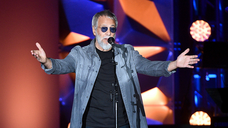 Yusuf Islam AKA Cat Stevens on stage, speaking into a microphone while gesturing.
