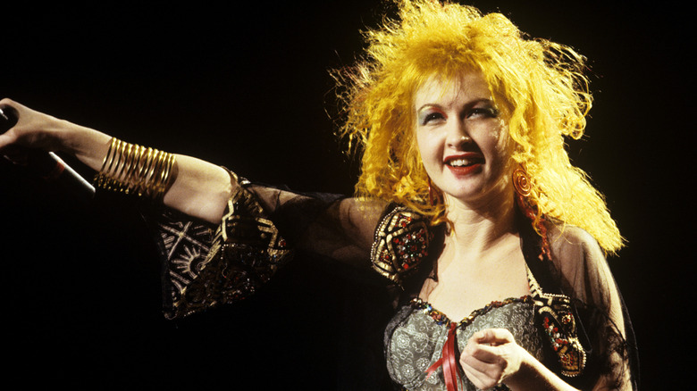 Cyndi Lauper smiling with arm outstretched on stage