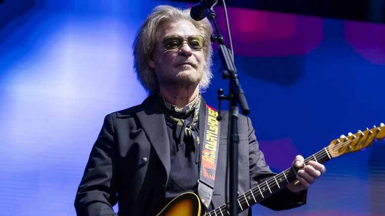 Daryl Hall playing guitar on stage in front of microphone